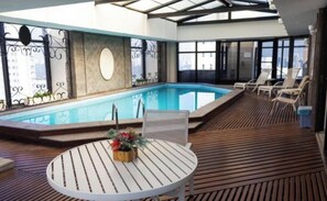 Ein Poolbereich auf dem Dach mit einer Holzterrasse, Liegestühlen und einem Tisch mit einer Blumenarrangememt.