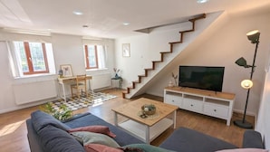 Un salon comprenant un canapé, une table basse, un téléviseur, un escalier et un bureau.