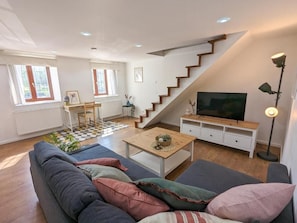 A living room with a sofa, a coffee table, a TV, a staircase, and a desk. - Stylish 2-Bedroom Apartment in Central Budapest (Budapest)