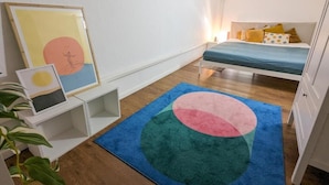 Une chambre à coucher comprenant un lit, une table de chevet, un climatiseur fixé au mur et un tapis coloré.