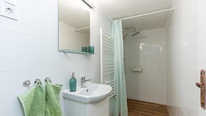 Une salle de bain équipée d’un lavabo, d’un miroir, d’un porte-serviettes, d’une douche et d’un tapis en bois.