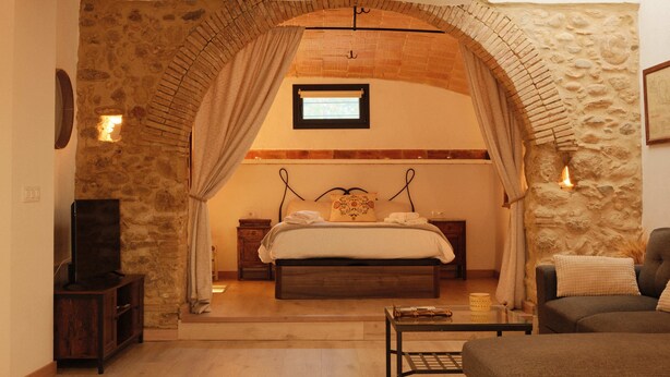 Une chambre avec une arche en pierre, un lit, une télévision et un canapé.