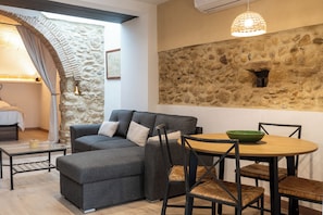 A modern living room with a stone wall, a gray sofa, a wooden dining table, and a green bowl. - Can Joan Loft - A romantic loft with a medieval arch on the Costa Brava (Ordis)