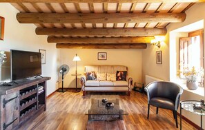 Un salon chaleureux avec un plafond en bois, un canapé, un téléviseur, une table basse en verre et une cheminée.