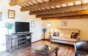 A living room with a wooden ceiling, a sofa, a glass coffee table, a TV, and a wine rack. - Country House with Vineyard Views, BBQ & Fireplace (El Pla del Penedès)