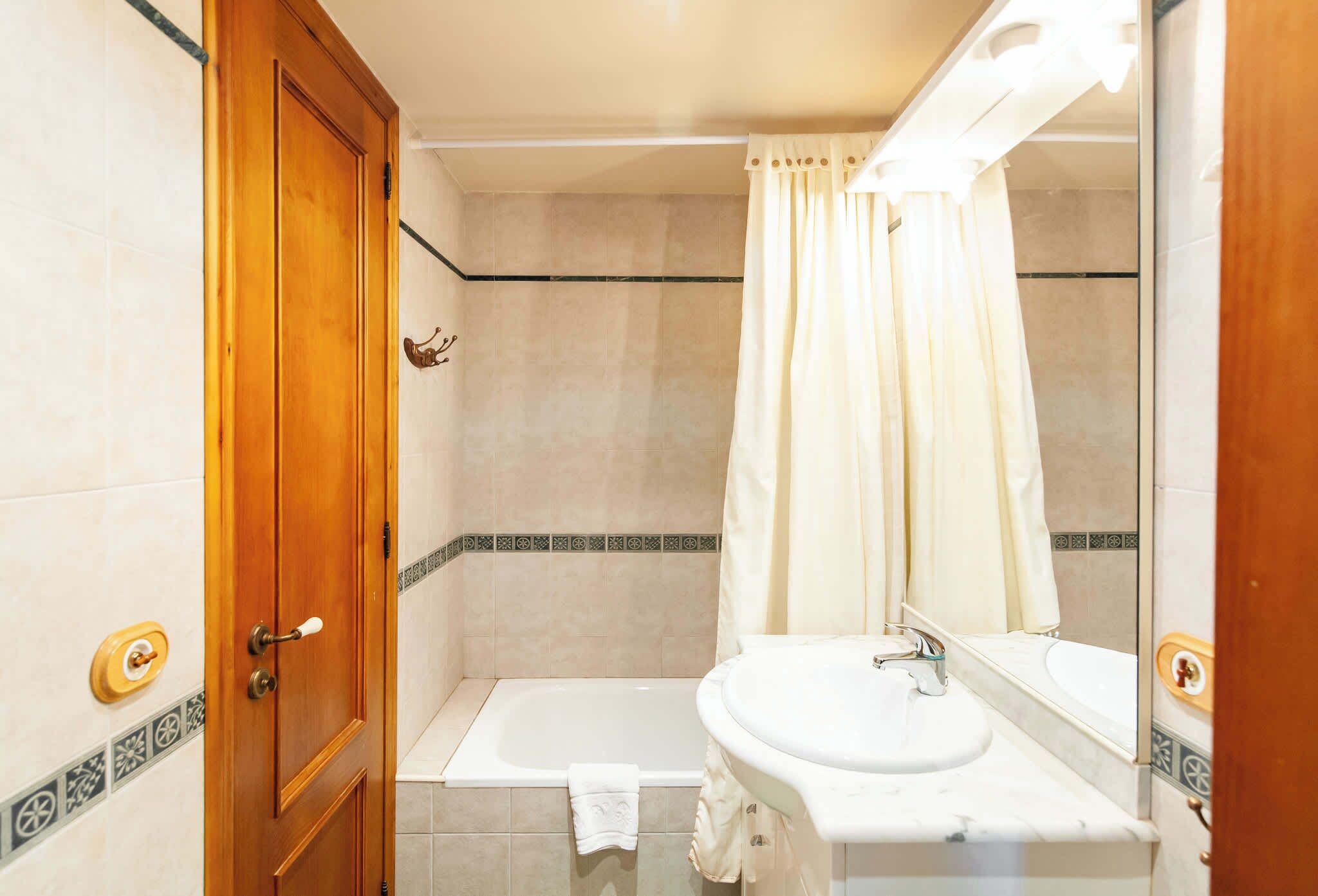 A bathroom with a wooden door, a bathtub, a sink, and a mirror.