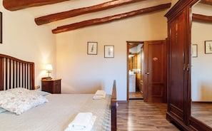 A bedroom with a bed, bedside table, lamp, wooden wardrobe, and framed pictures on the wall.