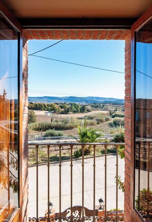 Un balcon offrant une vue sur un paysage rural, avec des champs et des collines à l’horizon.