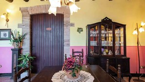 A dining area with a wooden table, a chandelier, a cabinet with glassware, and a door with a sign. - Vineyard-View Country House with BBQ & Fireplace (El Pla del Penedès)