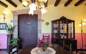 A dining area with a wooden table, chairs, a chandelier, a cabinet with glassware, and a door with a sign.