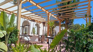 A covered outdoor patio with wooden beams, a table with chairs, and various plants. - Villa 6 Chambres 3 Suites, piscine chauffée. Prix 18 pax avec petits déjeuners. (Essaouira)