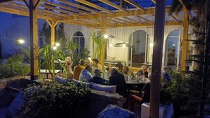 Ulkoterassi, jossa on puinen pergola, pyöreät pöydät ja ruukkukasveja.