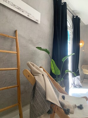 Una habitación con una escalera de madera, un sillón acolchado, una planta en maceta, una obra de arte en la pared y una ventana con cortinas.