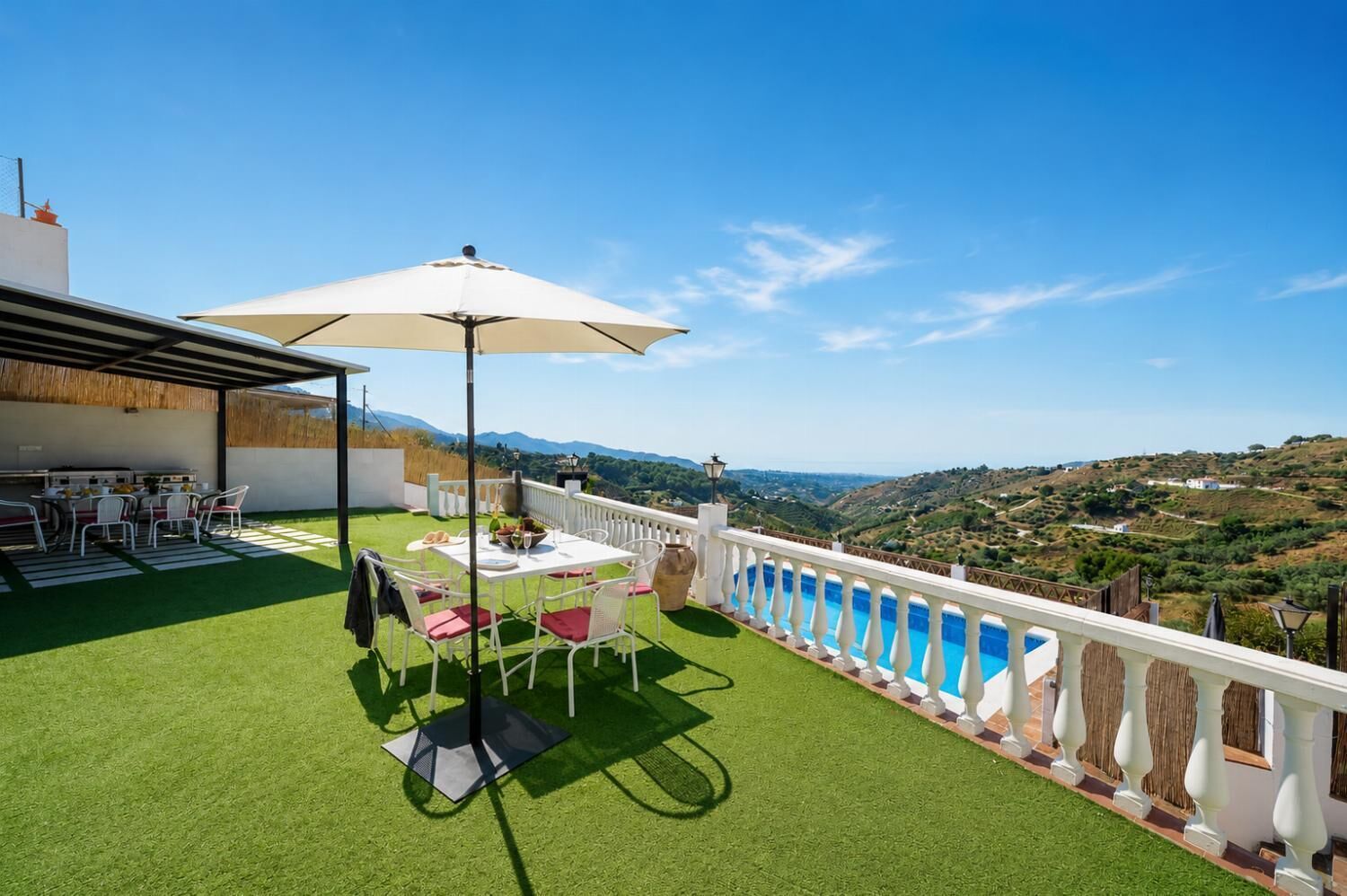 A terrace with a table and chairs, a white umbrella, and a view of a valley.