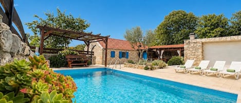 A swimming pool with lounge chairs, a pergola, and stone walls.