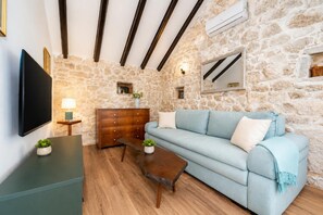 A living room with a stone wall, a wooden sofa, a TV, a wooden coffee table, and a small side table with a lamp. - Didini Dvori - One Bedroom Villa, Sleeps 2 (Kruševo)