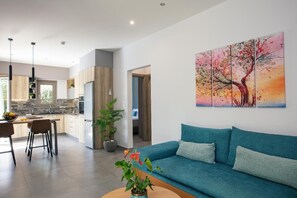 Ein modernes Wohnzimmer mit einem blauen Sofa, einem Couchtisch mit Pflanze und einer Küchenzeile mit Esstisch.