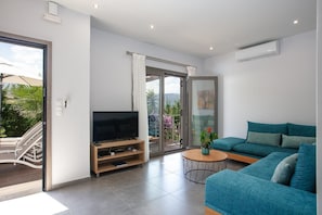 Ein modernes Wohnzimmer mit Flachbildfernseher, einer Couch, einem Couchtisch und einer Schiebetür zum Balkon.