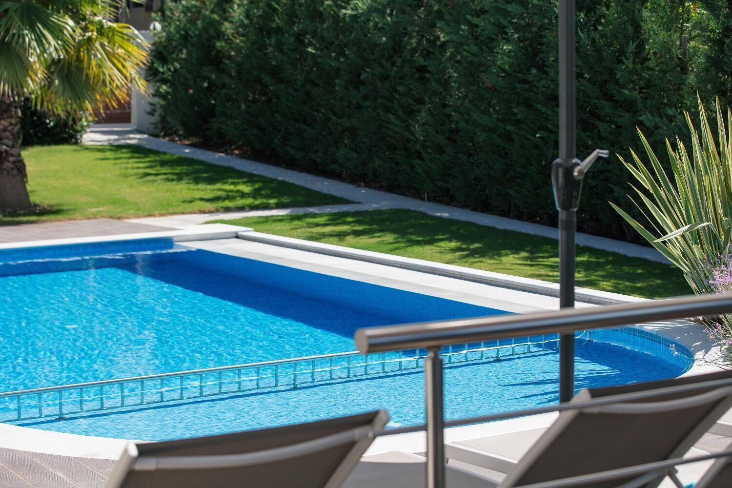 Une piscine entourée d’une rampe métallique, bordée d’une pelouse bien entretenue et de haies.