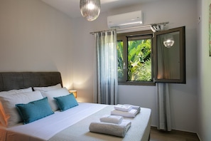 Ein Schlafzimmer mit Bett, Kissen, einem Fenster mit Vorhängen, einer Klimaanlage und einer Pendelleuchte.