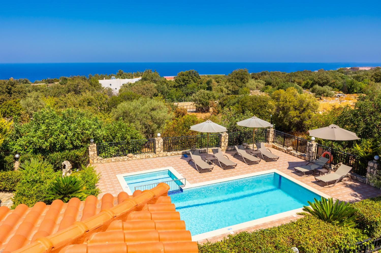 A swimming pool with lounge chairs and umbrellas, surrounded by greenery and overlooking a body of water.