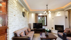 A living room with a brick wall, a sofa, a coffee table, a TV, and a fireplace. - Villa Nefeli Breeze - Three Bedroom Villa, Sleeps 6 (Rethymno)