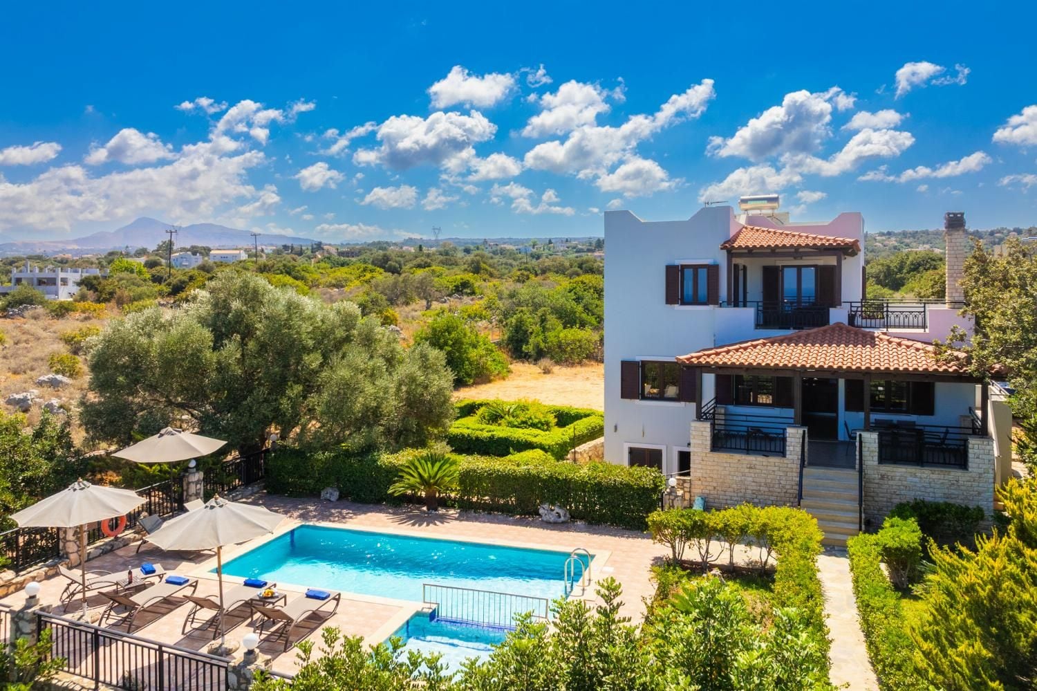 A modern two-story house with a swimming pool, surrounded by lush greenery and a clear blue sky.