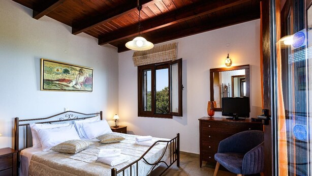 A bedroom with a bed, bedside table, lamp, window, dresser, chair, and a television. - Villa Nefeli Breeze - Three Bedroom Villa, Sleeps 6 (Rethymno)