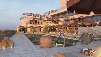 A rooftop pool area with lounge chairs, umbrellas, and a view of the ocean.