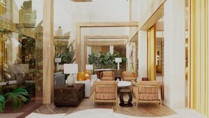 A room with a sofa, chairs, a coffee table, and a lamp. There are plants and a wooden structure in the background.
