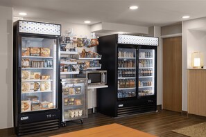 A kitchenette area with a microwave, refrigerator, and vending machines stocked with snacks and beverages.