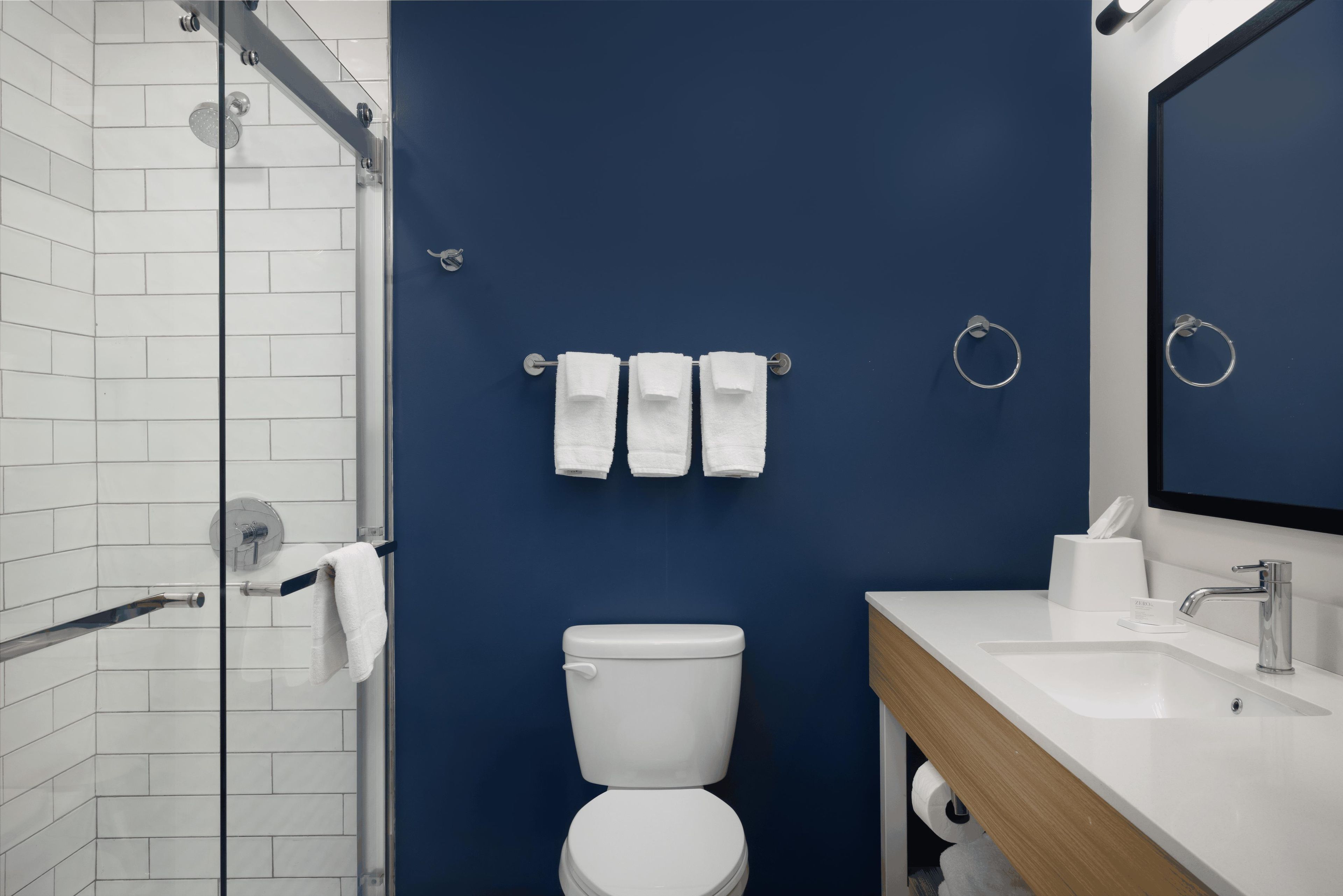 A bathroom with a white toilet, a sink, and a mirror. There are three white towels hanging on a towel rack.