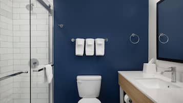 A bathroom with a white toilet, a sink, and a mirror. There are three white towels hanging on a towel rack.