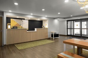 Un área de recepción con un mostrador de madera, una mesita auxiliar y una alfombra verde.
