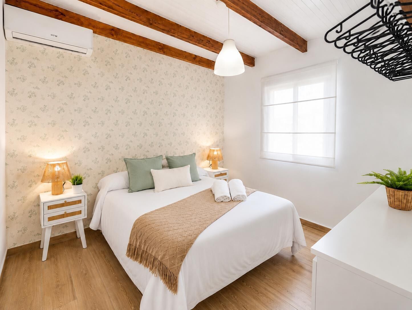 Un dormitorio con cama, lámparas de noche, mesita de noche, planta en maceta y ventana.