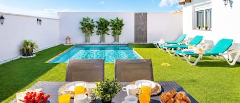 Un coin petit-déjeuner aménagé au bord de la piscine, avec une table, des chaises et la piscine elle-même.