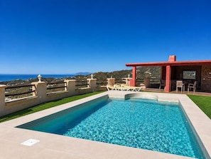 Ein Pool mit Liegestühlen, einer roten Pergola und Blick aufs Meer.