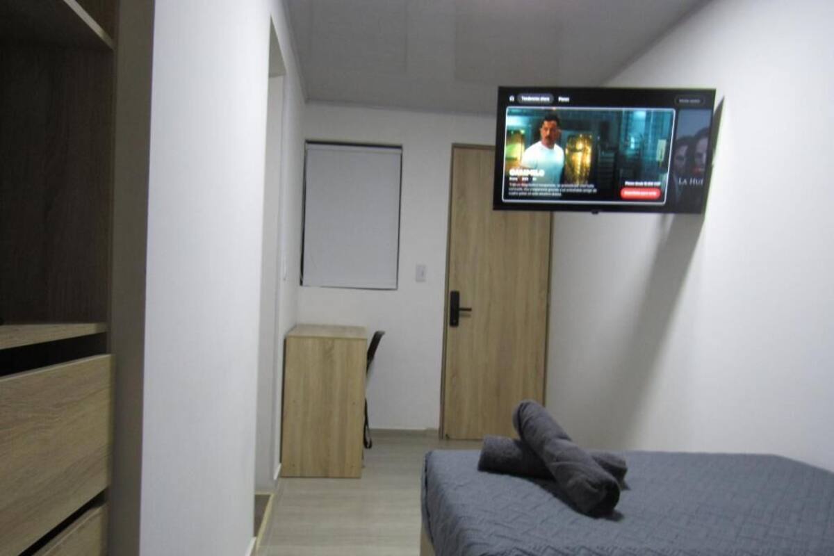 A bedroom with a bed, a television mounted on the wall, a wooden wardrobe, and a door.