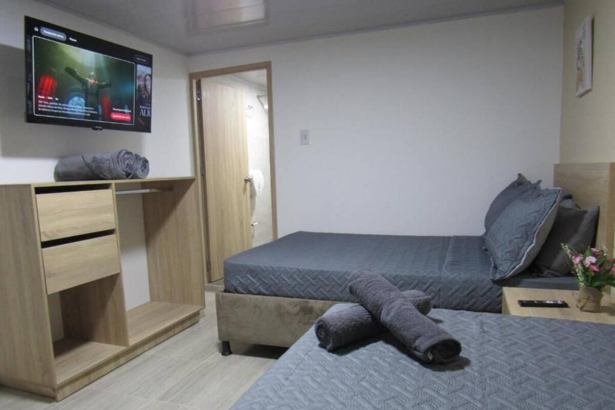 A bedroom with a bed, a desk, a TV, and a door.