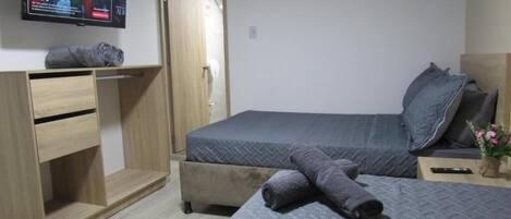 A bedroom with a bed, a desk, a TV, and a door.