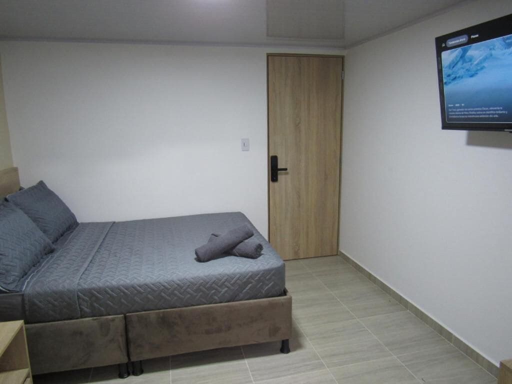Een slaapkamer met een bed, een houten deur en een aan de muur bevestigde televisie.