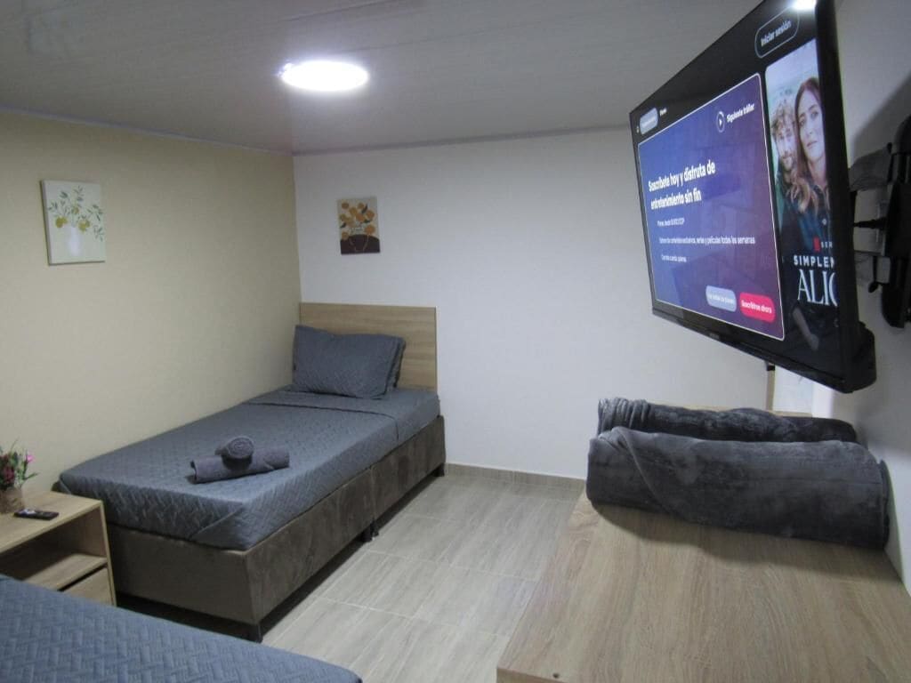 A room with a bed, a TV mounted on the wall, and a small table with a remote control.