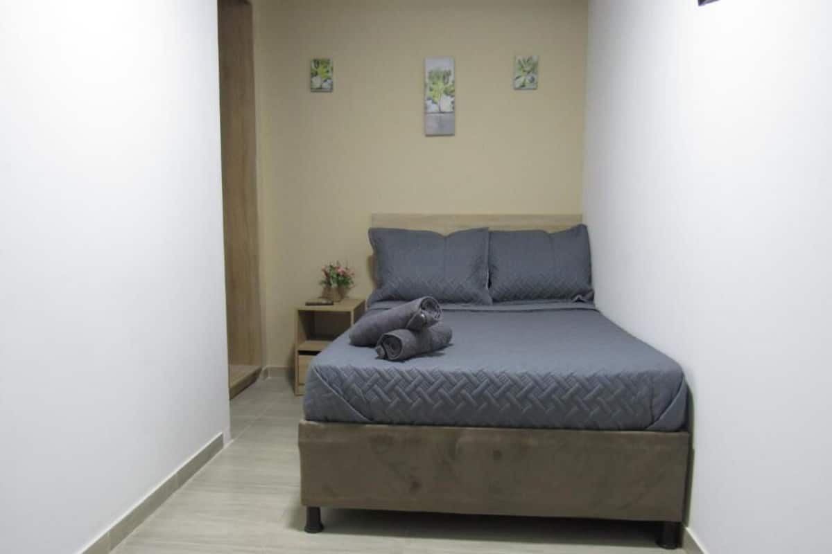 A bedroom with a bed, a nightstand, and a wall-mounted shelf.