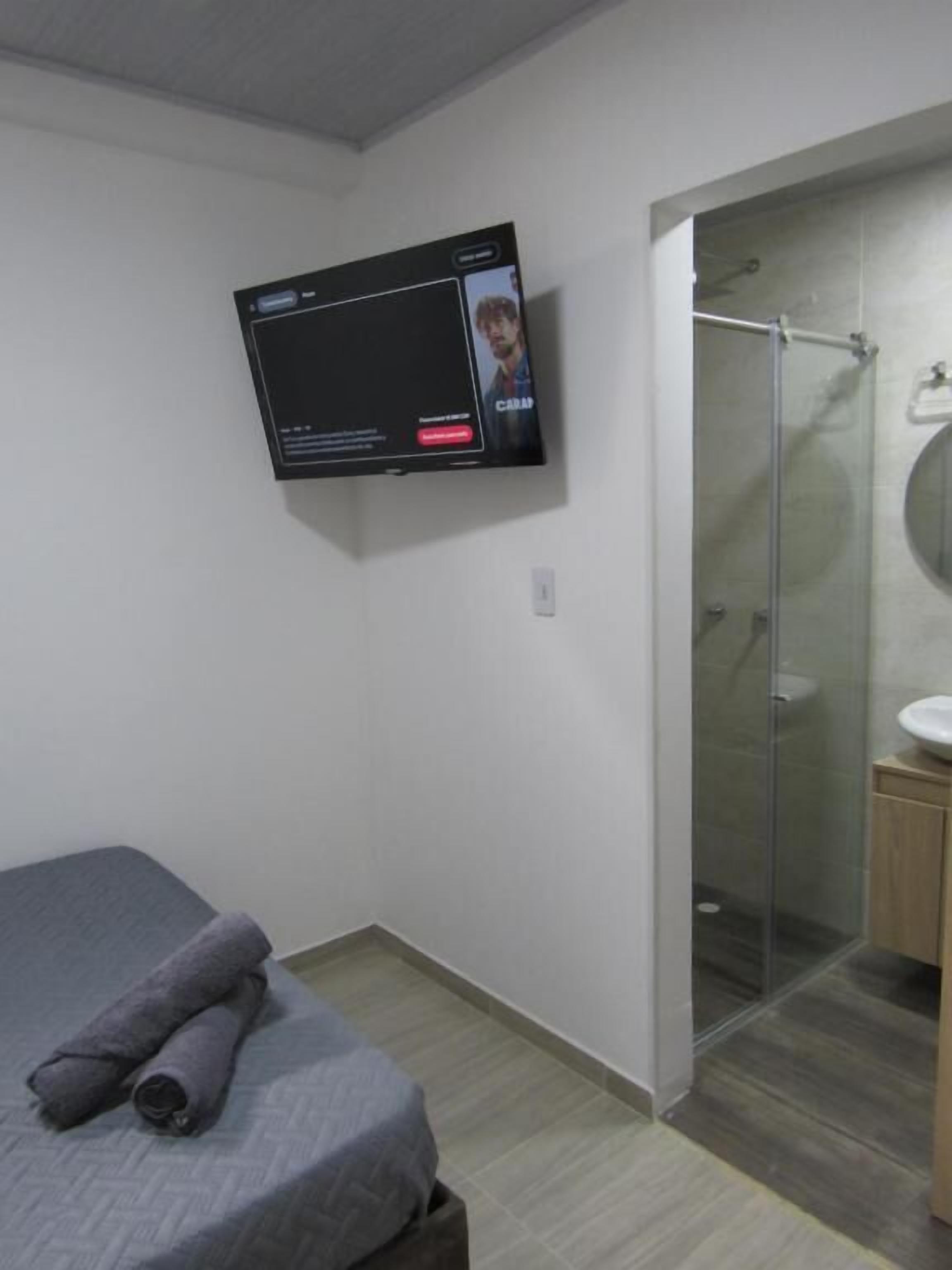 A bedroom with a bed, a television mounted on the wall, and a shower area with a glass door.