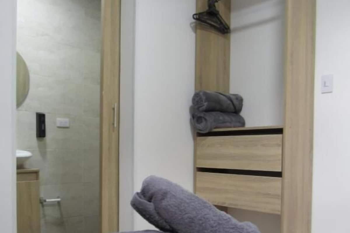 A bedroom with a bed, a wooden wardrobe, and a bathroom visible through an open door.