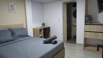 Un dormitorio con cama, escritorio, silla, armario y baño.