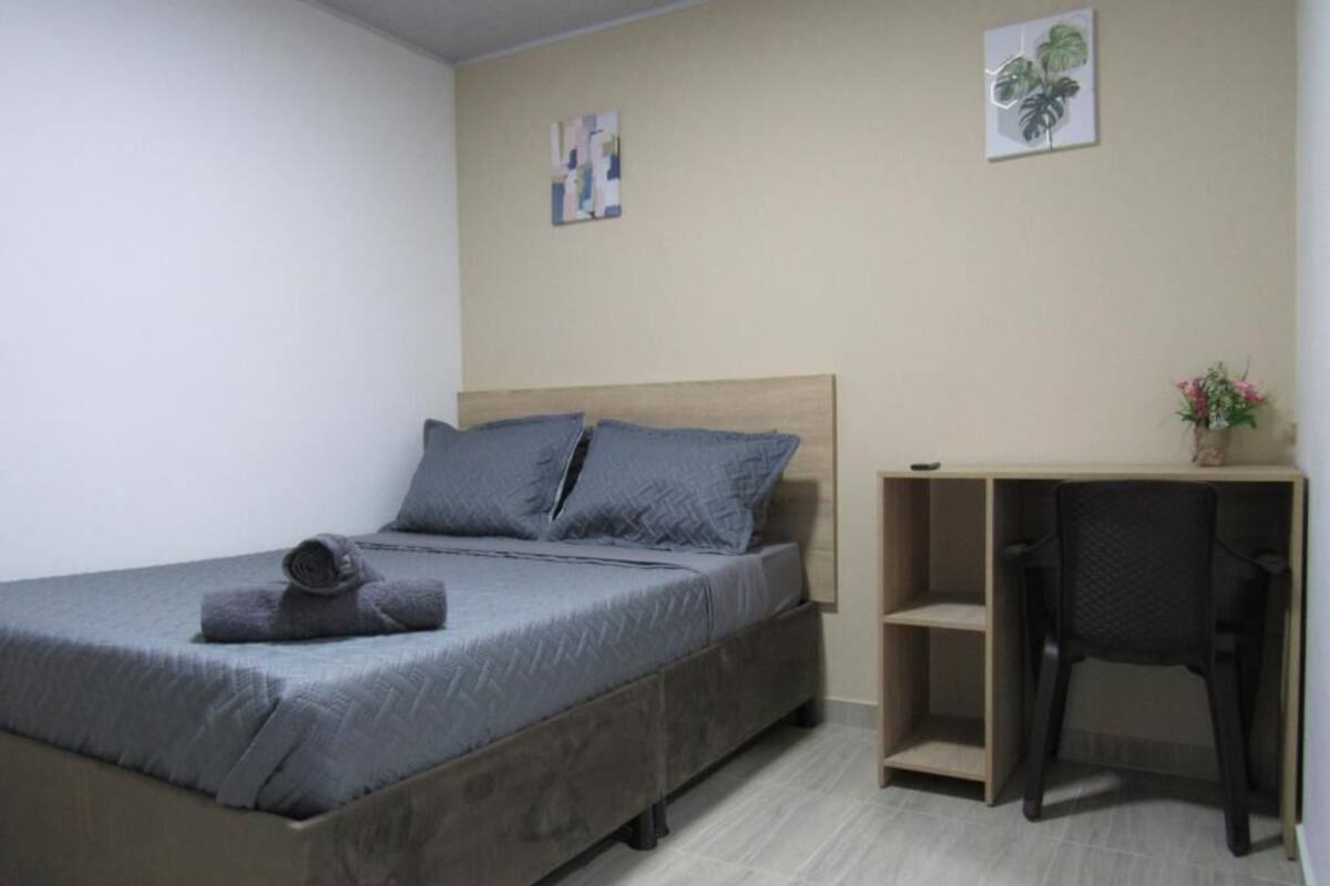 A single bed with a grey bedspread, a wooden headboard, and a small desk with a chair.