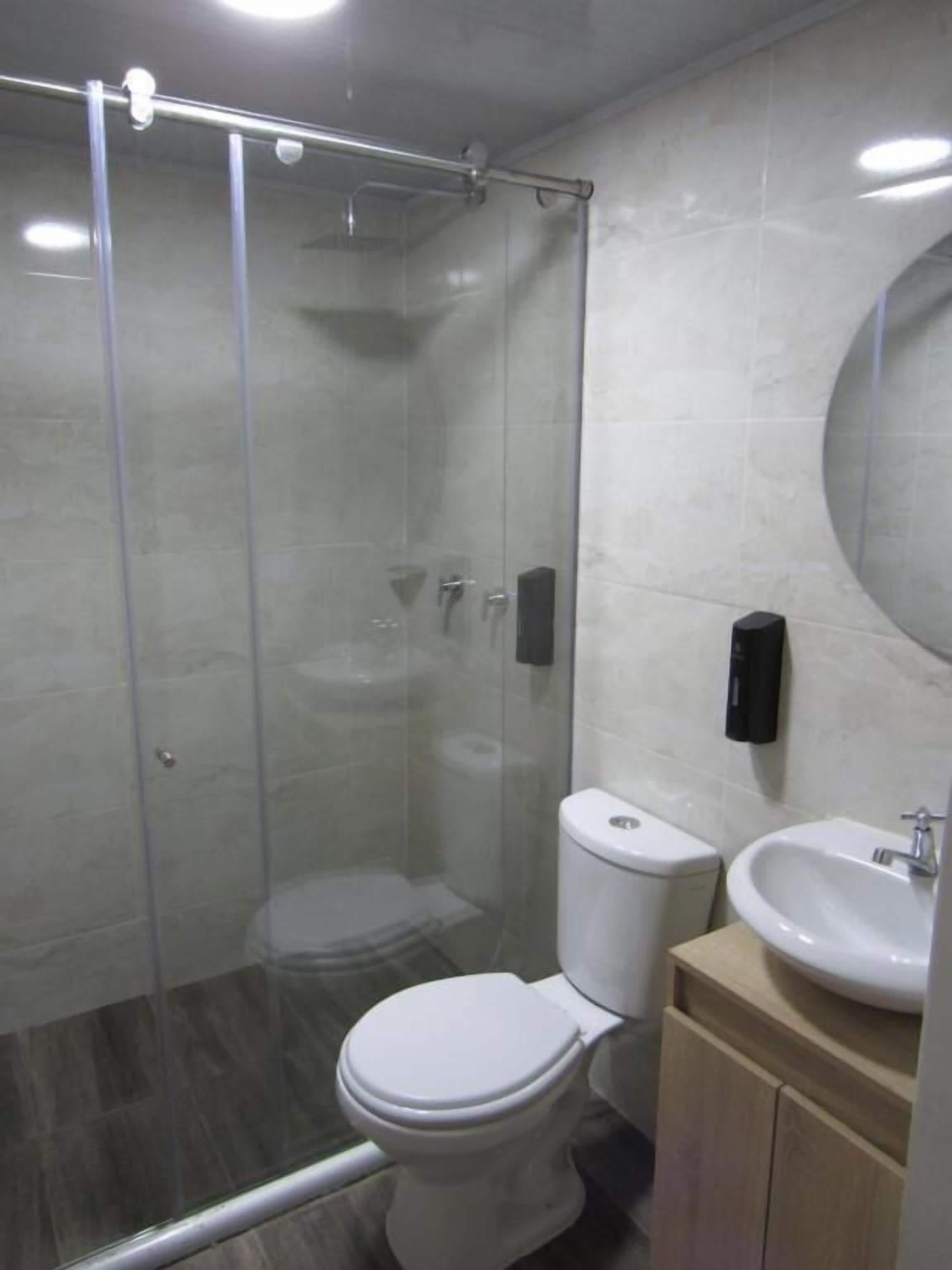 Een badkamer met een douchecabine van glas, een wit toilet, een wastafel en een spiegel.