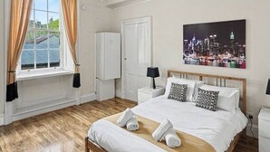 Une chambre d’hôtel avec un grand lit, un tableau représentant un paysage urbain, une vue sur la ville, une armoire et une fenêtre avec des rideaux.