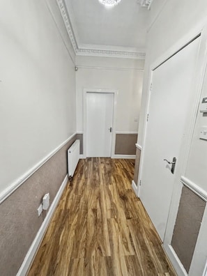 A hallway with wooden flooring, white walls, and a white door at the end.